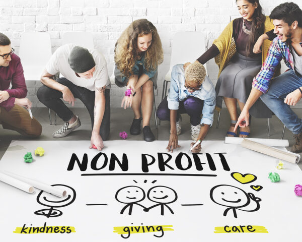 Diverse group of people collaborating on a nonprofit project, illustrating themes of kindness, giving, and care, with "NON PROFIT" prominently displayed in a creative setting.