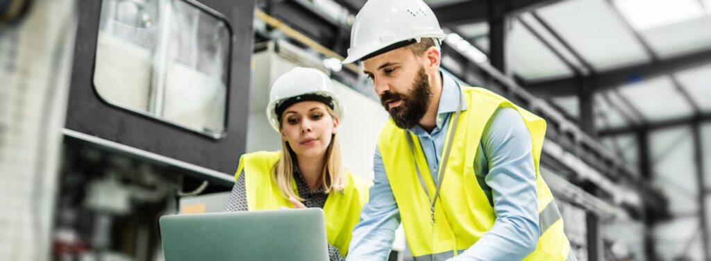 man and woman looking at a laptop in a manufacturing plant